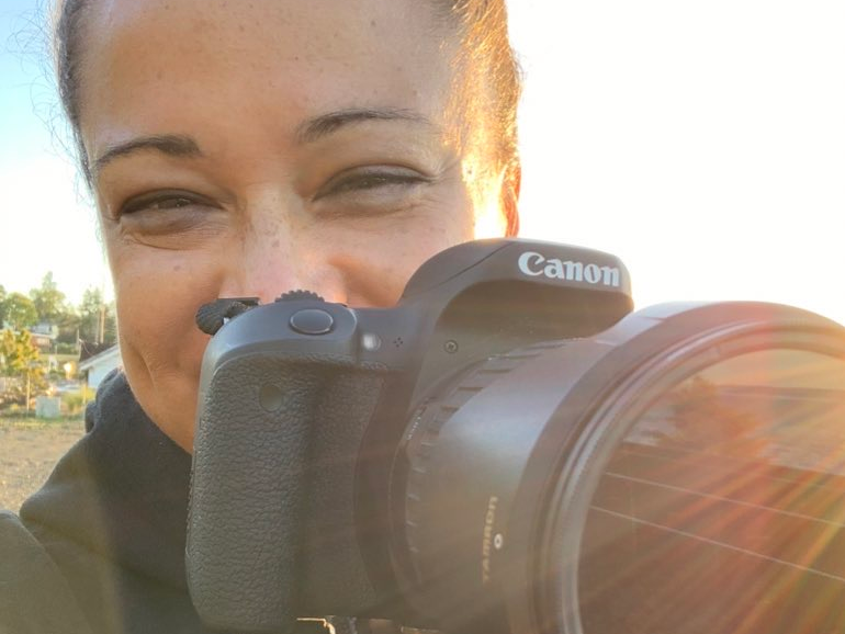 woman with dark brown hair and brown eyes sliming with a camera first image on her video editing services website